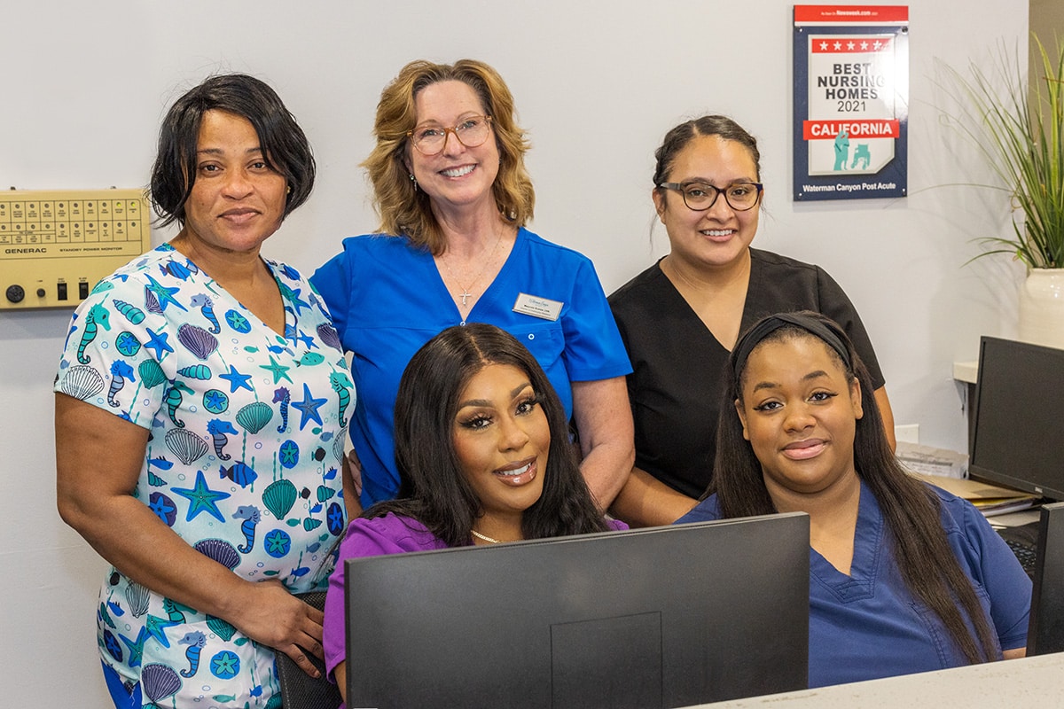 Five smiling female nurses behind a computer desk